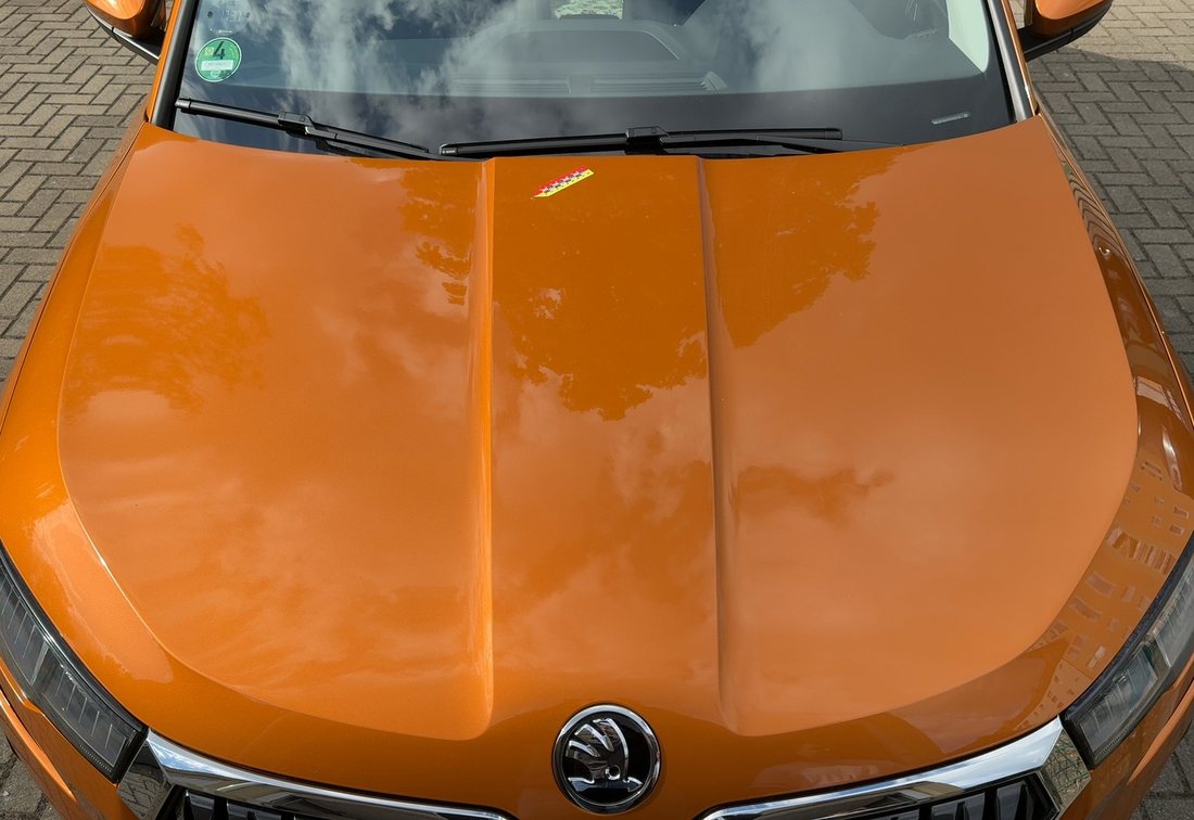 Motorhaube eines orangefarbenen Škoda Karoq mit Eindruckstelle vor der Windschutzscheibe, Schadengutachten über 3.256,91 €