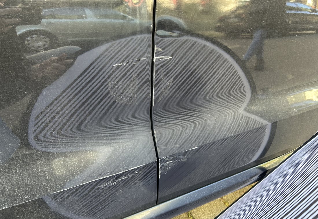 Eingedrückte Fahrer- und Fondtür eines schwarzen VW Polo, die Verformung zeichnet sich als Welle im Spiegelbild ab, wirtschaftlicher Totalschaden