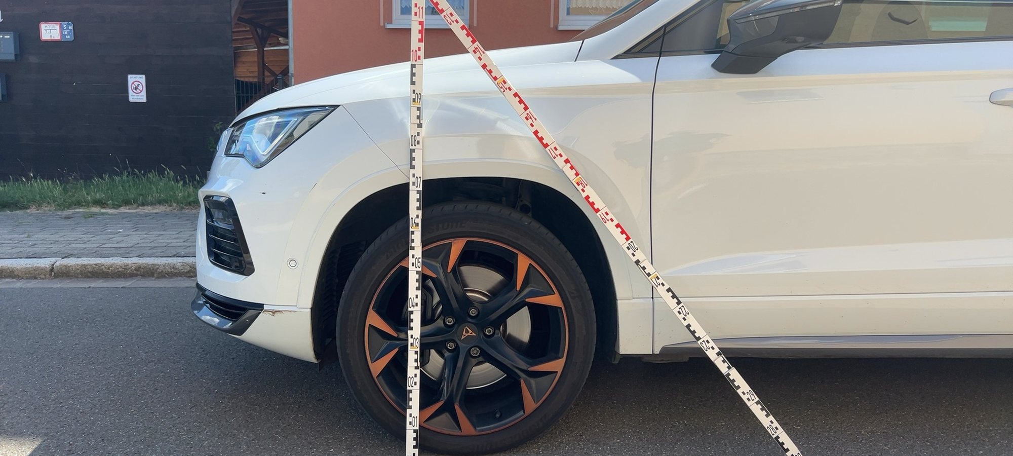 Kfz-Sachverständiger dokumentiert die Front eines weißen SUV mit zwei angelegten Messlatten